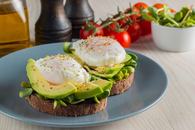 Avocado grzanka, czereśniowy pomidor i kłusujący jajka na drewnianym tle.