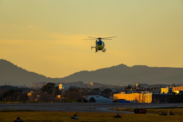 Awaryjni strażacy helikopterów z ostatnimi godzinami zachodzącego słońca wykonują manewry lądowania na pasie startowym lotniska Sabadell z hangarami górskimi i złotym niebem na horyzoncie