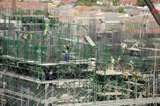 Azjaci i tajscy pracownicy z ciężkimi maszynami pracującymi konstruktora nowy budynek na budowie wieżowiec na rusztowaniu w stolicy w Bangkoku Tajlandia