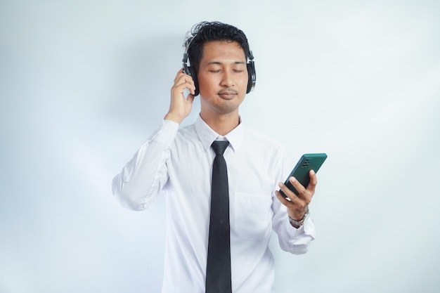 Azjat cieszy się muzyką z telefonu komórkowego za pomocą bezprzewodowych słuchawek izolowanych na białym