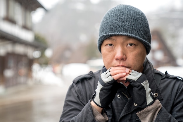 Azjata w śnieżnym kapeluszu wpatruje się w kamerę i myśli coś, dolina Shirakawako w tle sezonu śnieżnego.