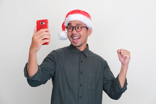Azjata w świątecznym kapeluszu, podekscytowany, patrząc na swój telefon