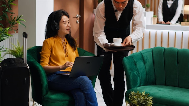 Azjatka bierze kawę, pracując na laptopie.