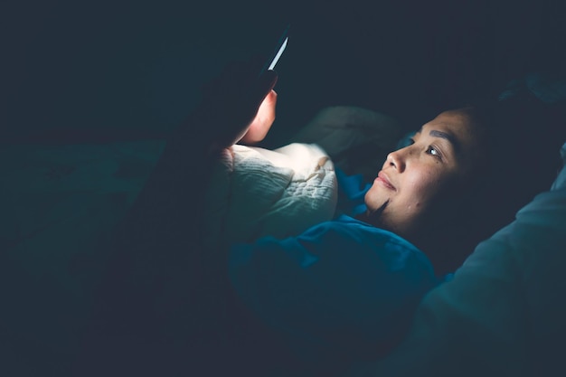 Azjatka gra w nocy na smartfonie w łóżku Ludzie z TajlandiiAddict social mediaGraj w internet przez całą nocLychnobite