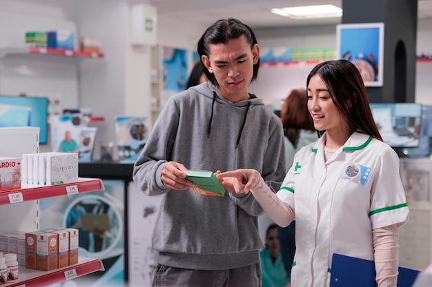 Azjatka i konsultant rozmawiają o pudełku z witaminami i wyjaśniają ulotkę suplementów w aptece. Farmaceuta dający pakiet leków i środków medycznych, pomoc w aptece.