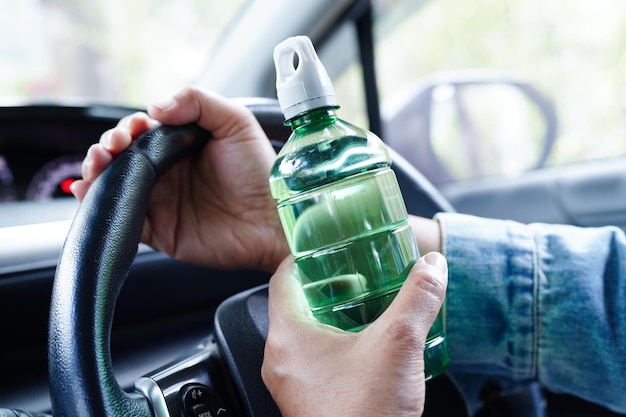 Zdjęcie azjatka kierowca trzyma zimną wodę do picia w samochodzie niebezpieczna i ryzyko wypadku
