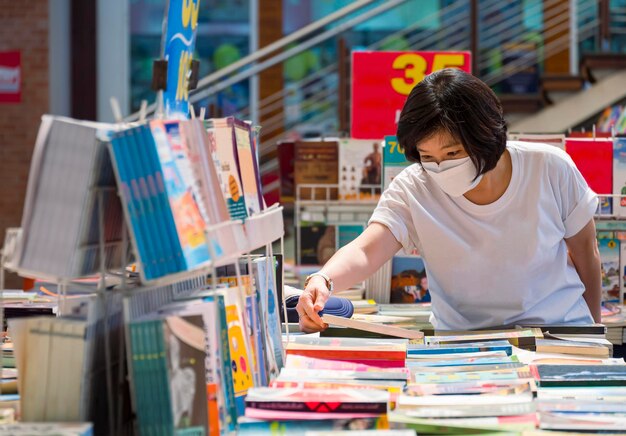 Azjatka nosi maskę ochronną i wybiera książki w księgarni w centrum handlowym