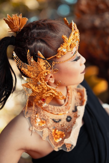Azjatka pozuje z ręką w czarnej sukience i złotym pasku ze złotą koroną na głowie