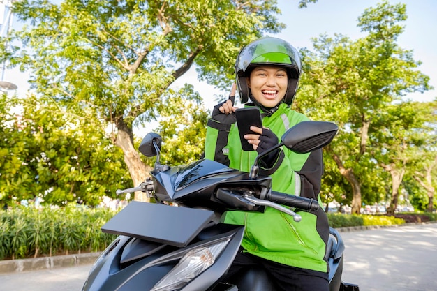 Azjatka pracuje jako taksówkarz motocyklowy, sprawdzając zamówienie na swoim telefonie komórkowym