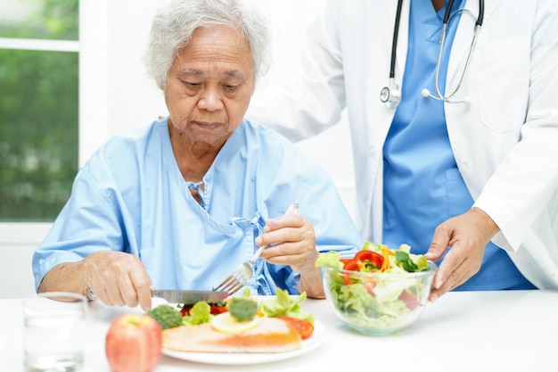 Azjatka, starsza pacjentka, jedząca łososia i sałatkę warzywną jako zdrowe jedzenie w szpitalu