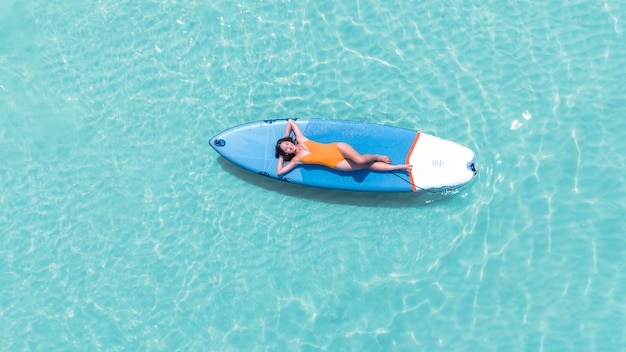 Azjatka w bikini śpi i relaksuje się na desce wiosłowej na plaży latem na plaży Pattaya