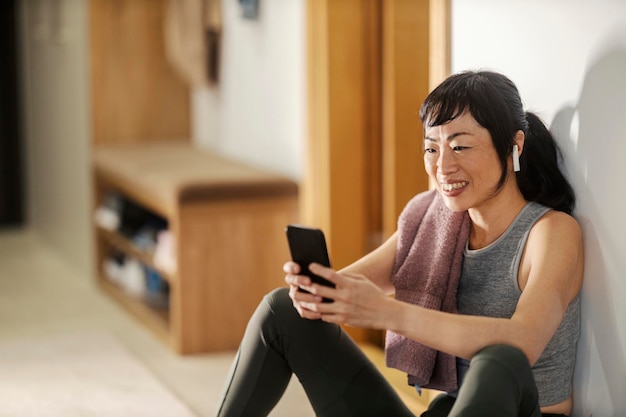 Azjatka w średnim wieku uśmiecha się do telefonu po ćwiczeniach w domu