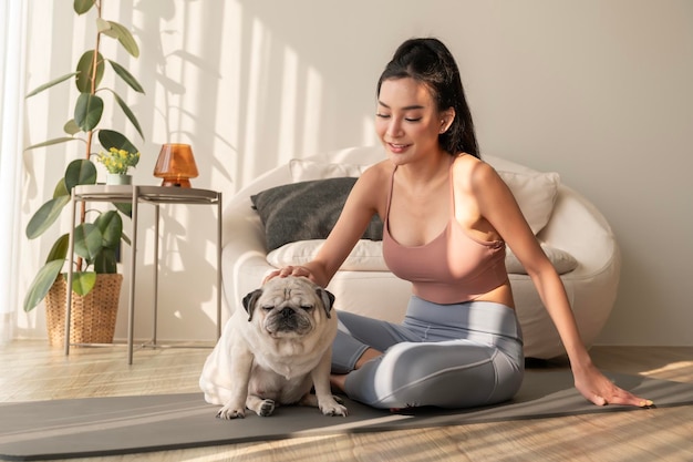 Azjatka w stroju sportowym ćwiczy i robi jogę z uroczym psem w salonie.