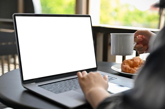 Azjatka zdalna pracująca w kawiarni, popijająca kawę podczas pracy na laptopie