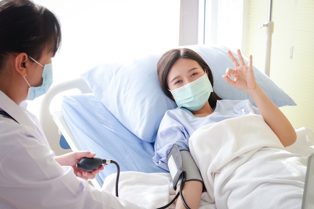 Azjatki Nosić niebieską maskę i leżeć na szpitalnym łóżku. Podnieś rękę. w porządku