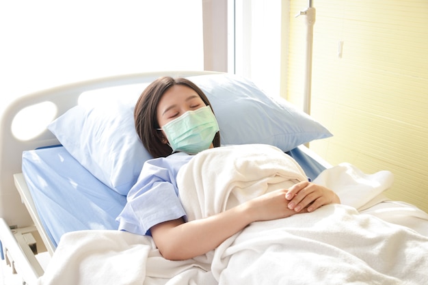 Azjatki Noszą niebieską maskę i leżą w szpitalnym łóżku