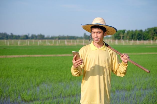 Azjatyccy rolnicy mężczyzna noszą żółte koszule za pomocą smartfona w zielonej farmie.
