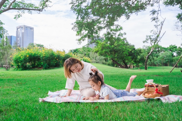 Azjatycka babcia i wnuczka kłaść na zielonego szkła polu plenerowym, rodzinny cieszy się piknik wpólnie w letnim dniu