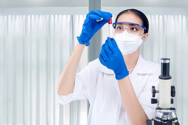 Azjatycka badaczka z maską na twarz i okularami trzymająca rurkę medyczną w laboratorium