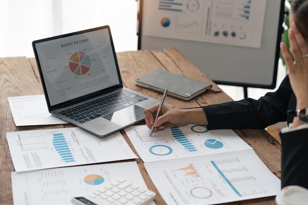 Azjatycka biznesmenka siedzi przy biurku w biurze i oblicza wykresy finansowe przedstawiające wyniki dotyczące ich inwestycji planujących udane diagramy procesów rozwoju biznesu na ekranie