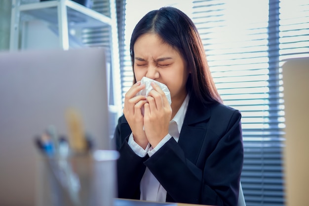Azjatycka Biznesowa Kobieta Używa Papierową Serwetkę Usta I Nos Ponieważ Alergia W Stole Na Biurowym Pokoju.