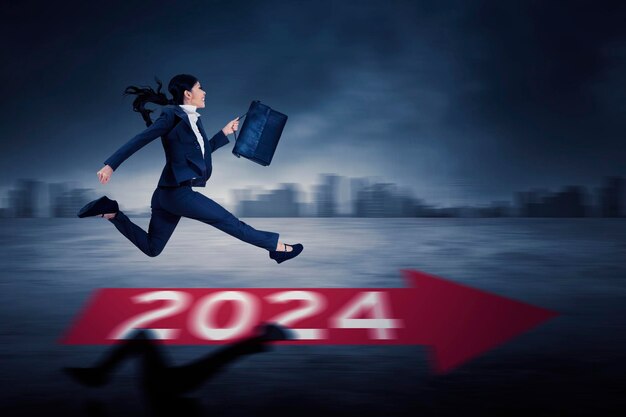 Azjatycka bizneswoman biegnie w kierunku przyszłości z numerami nowego roku 2024 na ziemi
