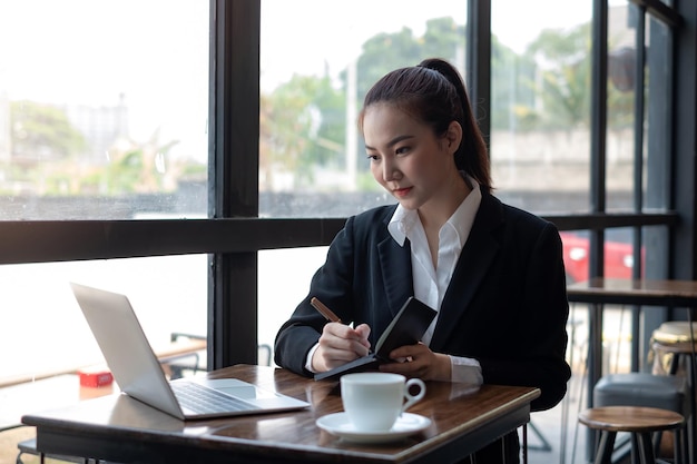 Zdjęcie azjatycka bizneswoman pracuje na laptopie z robieniem notatek z pracy w biurze