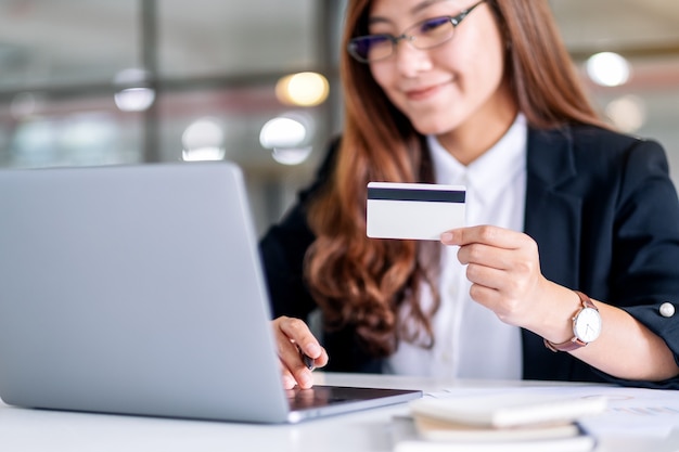 Azjatycka bizneswoman trzymająca karty kredytowe podczas korzystania z laptopa w biurze