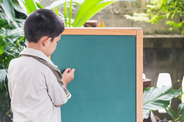 Azjatycka chłopiec punktów ręka pisze na blackboard