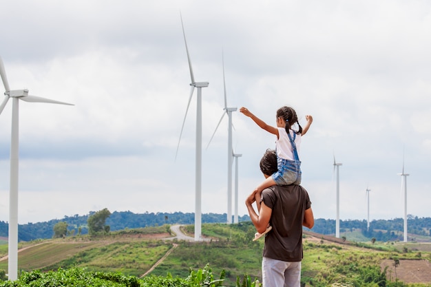 Azjatycka dziecko dziewczyna jedzie na ojców ramionach w turbina wiatrowa polu