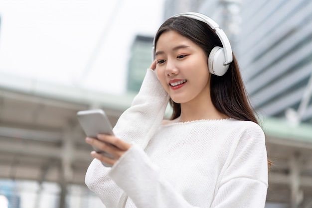 Azjatycka dziewczyna jest ubranym hełmofony słucha transmitować muzykę z mądrze telefonu