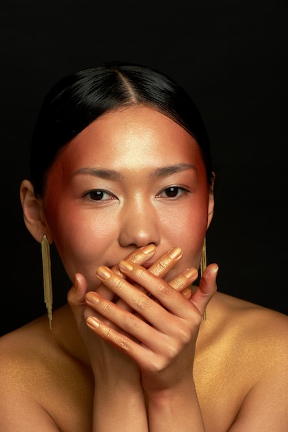 Azjatycka dziewczyna na czarnym tle w studio Złoto ukrywa uśmiech