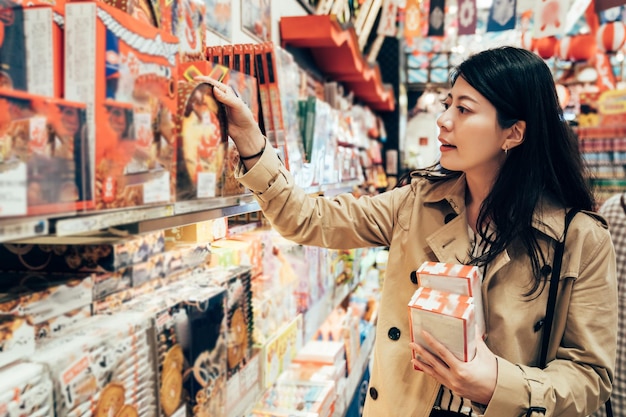 Azjatycka dziewczyna podróżująca w podróży służbowej odwiedzająca lokalny specjalistyczny sklep w dotonbori osaka japonia wybierająca pamiątkę dla rodziny. młoda dama patrząc trzymając japońskie ciasteczko w sklepie.
