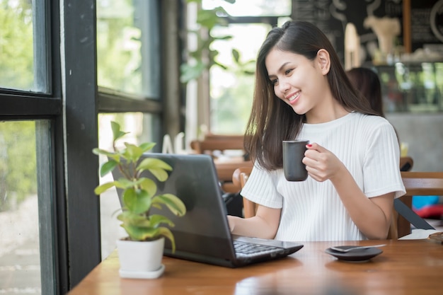 Azjatycka dziewczyna pracuje przy kawiarnią z laptopem i ma kawę