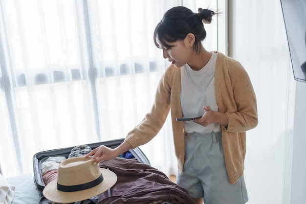 Zdjęcie azjatycka dziewczyna przygotowuje wakacje w sypialni kobieta robi listę kontrolną przed wakacyjnym wyjazdem