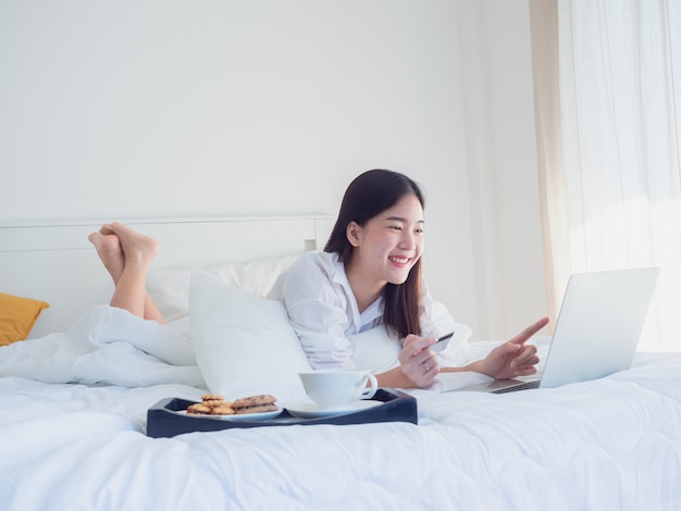Azjatycka Dziewczyna Używa Komputer Z Kredytową Kartą Na łóżku