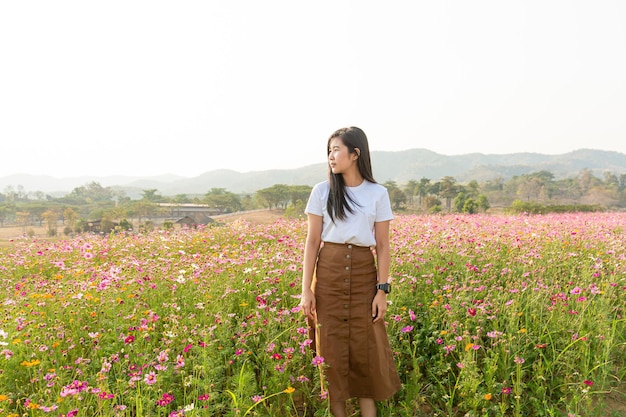 Azjatycka dziewczyna w białej sukni siedzi na łące z różowymi kwiatami na wsi
