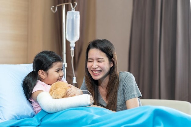 Azjatycka dziewczyna ze złamaną ręką nosząca gips na szpitalnym łóżku z matką