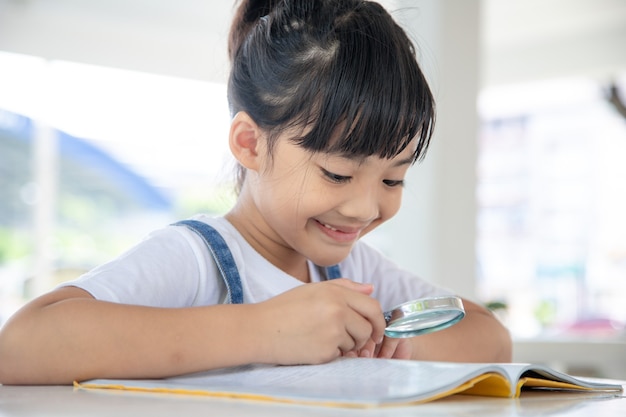 Azjatycka dziewczynka czytająca książki na biurku przez lupę