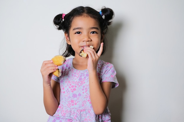 Azjatycka dziewczynka pokazująca szczęśliwy wyraz podczas jedzenia pączka