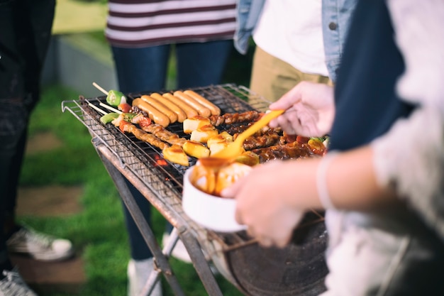 Azjatycka grupa przyjaciele robi grillowi i piec na grillu szaszłykom na rusztowym przyjęciu w plenerowym ogródzie