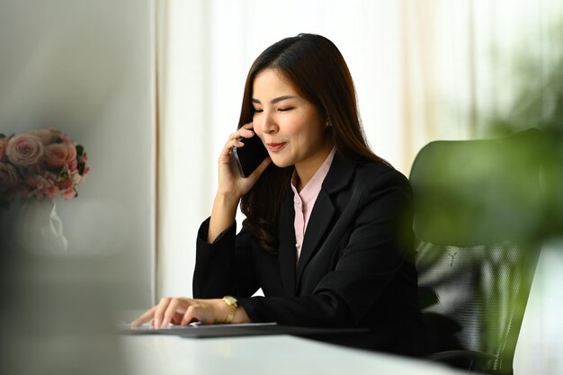 Zdjęcie azjatycka inwestorka rozmawiająca przez telefon komórkowy negocjująca z partnerem biznesowym nowoczesne miejsce pracy