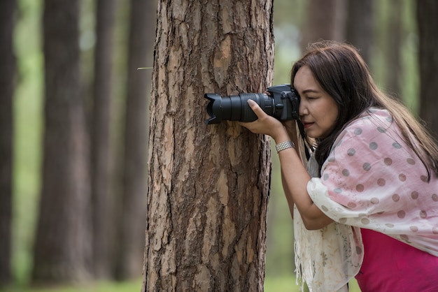 Azjatycka kobieta bierze fotografię z DSLR, strzela pozę z drzewnym pojęciem.