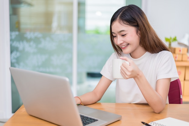 Azjatycka kobieta cieszy się podczas gdy używać laptopy i internet w biurze