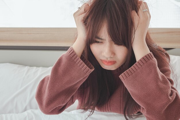 Azjatycka kobieta czuje bóle głowy i dyskomfort na łóżku w białej sypialni rano