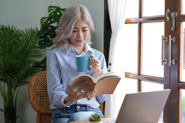 Azjatycka kobieta czytająca książkę i pijąca kawę rano