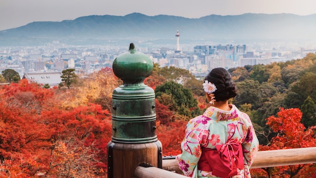 Zdjęcie azjatycka kobieta jest ubranym pięknego kimonowego odprowadzenie i podróżuje w japońskim ogródzie wśrodku świątyni z czerwonymi liśćmi klonowymi na jesieni.