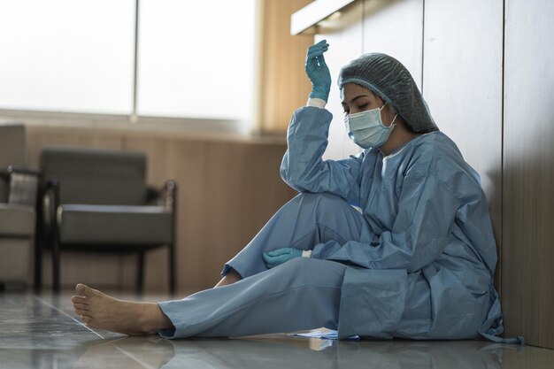 Azjatycka kobieta lekarz nosi chirurgiczną maskę na twarz, siedząc na podłodze, zmęczona pracą, ponieważ wpływ epidemii pandemii covid19 smutek pracownik opieki zdrowotnej kobieta koncepcja medyczna i opieki zdrowotnej