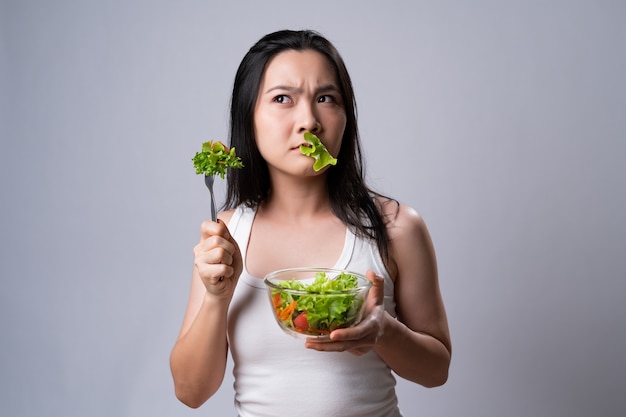 Azjatycka kobieta mylić z jedzeniem sałatki na białym tle nad białą ścianą. Zdrowy styl życia z koncepcją czystej żywności.