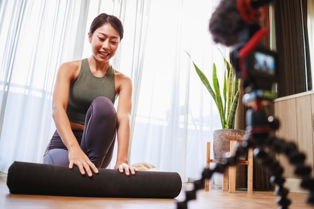 Azjatycka kobieta nauczycielka jogi filmuje zajęcia jogi online na wideo dla mediów społecznościowych Profesjonalny instruktor w odzieży sportowej pozuje na kamerze wideo Technologia zdrowego stylu życia w domu Nowy normalny styl życia